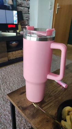 a pink coffee cup sitting on top of a wooden table next to a bowl of bananas