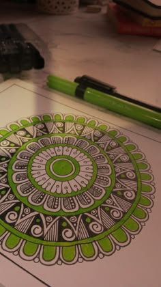 a green and white circular design on a piece of paper next to some markers, pens and pencils