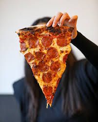 a woman holding up a slice of pepperoni pizza