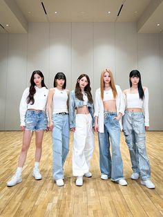 four young women standing in front of a wall wearing white tops and jeans, all looking at the camera