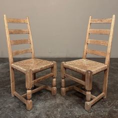 two wooden chairs sitting next to each other on top of a cement floor in front of a wall