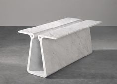 a white marble bench sitting on top of a cement floor next to a gray wall