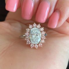 a woman's hand holding a ring with an oval diamond in the center and pink nail polish