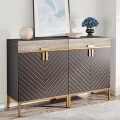 a black and gold sideboard with an art piece on top, next to a blue vase