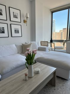 a living room filled with white furniture next to a large window covered in pictures on the wall