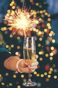 a person holding a wine glass with a sparkler in the middle of it and a christmas tree in the background