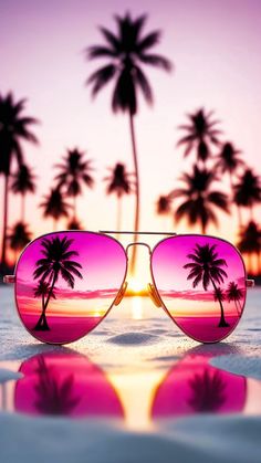 a pair of sunglasses with palm trees reflected in the lens, on a beach at sunset