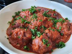 meatballs with sauce and parsley in a white bowl