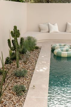 a pool with rocks and plants in it next to a white couch that has pillows on it