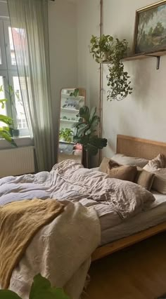 an unmade bed in a bedroom next to a window with potted plants on it