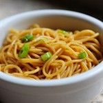 a white bowl filled with noodles and green onions on top of a table next to a fork