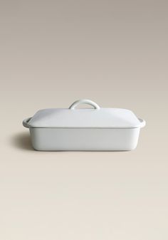 a white casserole dish sitting on top of a beige surface with an oval handle