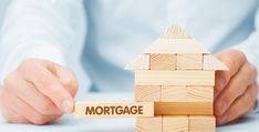 a person holding wooden blocks with the word mortgage on them and a house shaped like a block