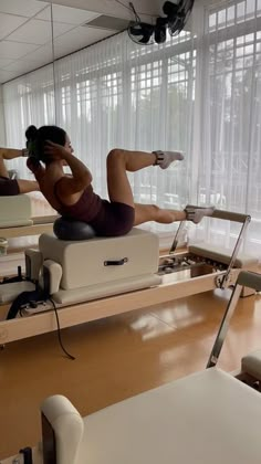 a woman is doing exercises on a stationary rowing machine in a room with large windows