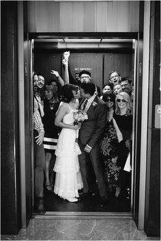 a bride and groom kissing in an elevator surrounded by their wedding party members, all dressed in black and white