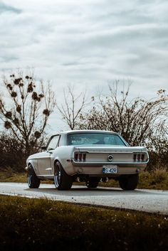 an old car is parked on the side of the road in front of some trees