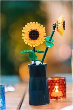 two sunflowers are placed in a vase on a table next to some candles