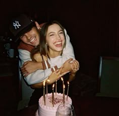 two people hugging each other in front of a birthday cake with lit candles on it