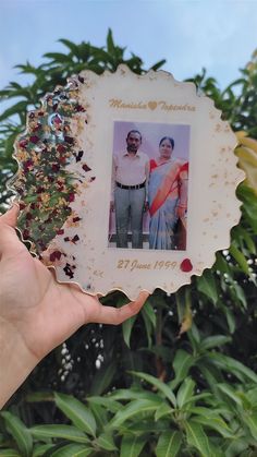 a person holding up an old photo in front of some trees and bushes with leaves on it