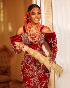 a woman in a red and gold dress holding a long feathered stick with beads on it