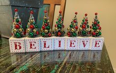 a table topped with small christmas trees on top of blocks that spell out the word believe