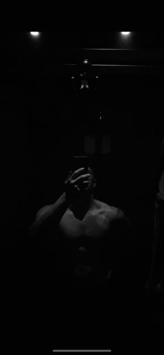 a shirtless man in the dark holding his hands to his face