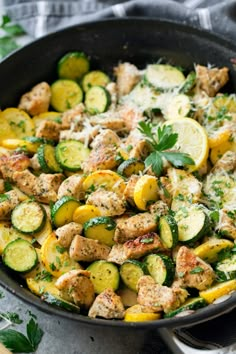 a skillet filled with chicken, zucchini and lemons on top of a table