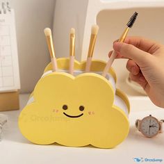 a person holding a toothbrush in front of a yellow cloud shaped holder with smiley faces on it