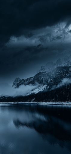 the mountains are covered in fog and clouds as they sit on top of a lake