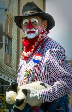 a clown with painted face holding a stuffed animal