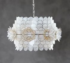 a white chandelier hanging from a metal chain with flowers on it, against a gray background