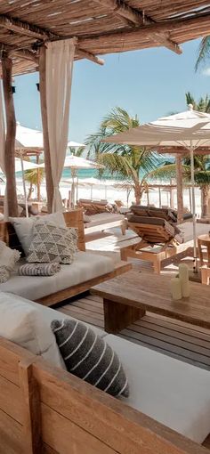 an outdoor seating area with wooden tables and umbrellas on the beach in front of palm trees