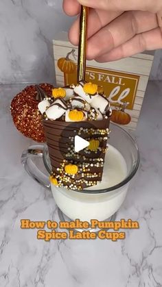 a person is holding a spoon over a cup filled with chocolate and marshmallows