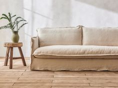 a white couch sitting on top of a wooden floor next to a potted plant