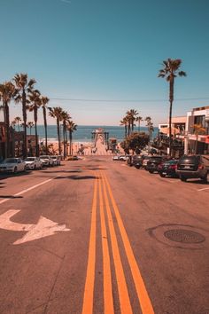 an empty street lined with palm trees next to the ocean