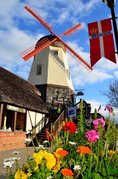 a windmill with flowers in the foreground and a flag hanging from it's side