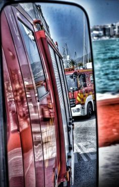 the reflection of a firetruck in a rear view mirror on a street next to water