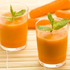 two glasses filled with orange juice and garnished with mints on a bamboo mat