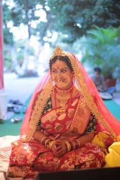 a woman sitting on top of a bed wearing a red and gold wedding outfit with jewelry