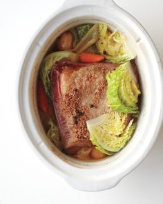 a pot filled with meat and vegetables on top of a white table next to a spoon