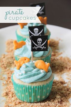 cupcakes decorated with blue frosting and pirate flags are on a white plate