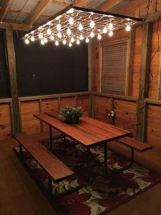 a wooden table and benches in a room with lights hanging from the ceiling above it