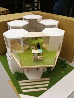 a model of a house with grass on the ground and people sitting at tables in front of it