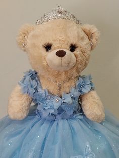 a brown teddy bear wearing a blue dress and tiara sitting on top of a table