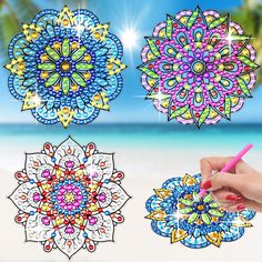 four different colored designs on the beach with a person holding a pen in their hand