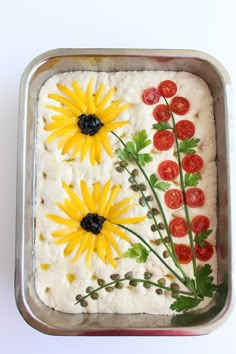 a cake decorated with sunflowers and tomatoes in a metal pan on a white surface