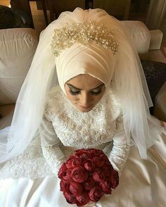 a woman in a wedding dress holding a bouquet of flowers on her lap, wearing a turban and veil