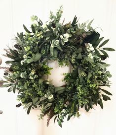 a wreath with green leaves and white flowers hanging on a door handle in front of a wall