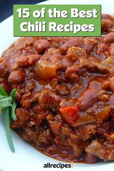 a white plate topped with chili and meat next to a green leafy garnish