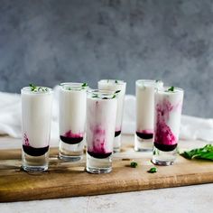 three glasses filled with liquid sitting on top of a cutting board next to mint leaves